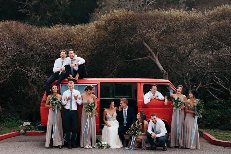 A wedding party poses in front of and on top of a red VW van.