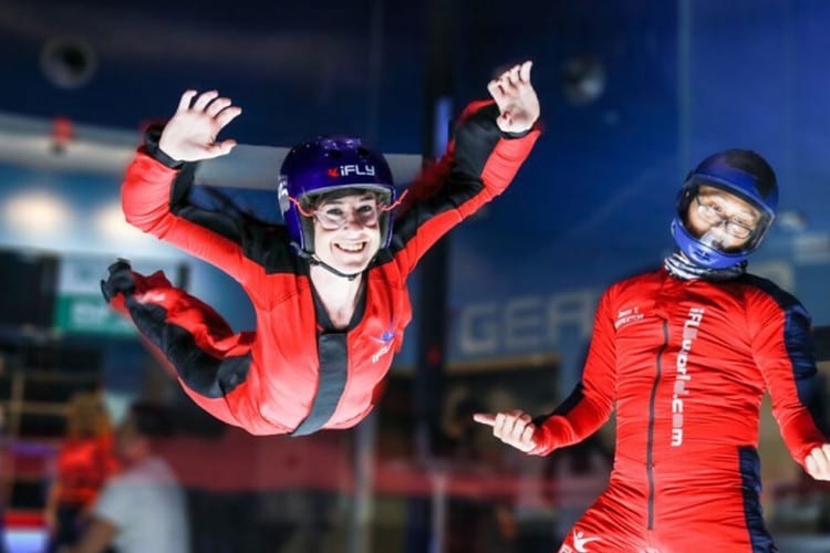 A woman tries indoor skydiving while her boyfriend looks on