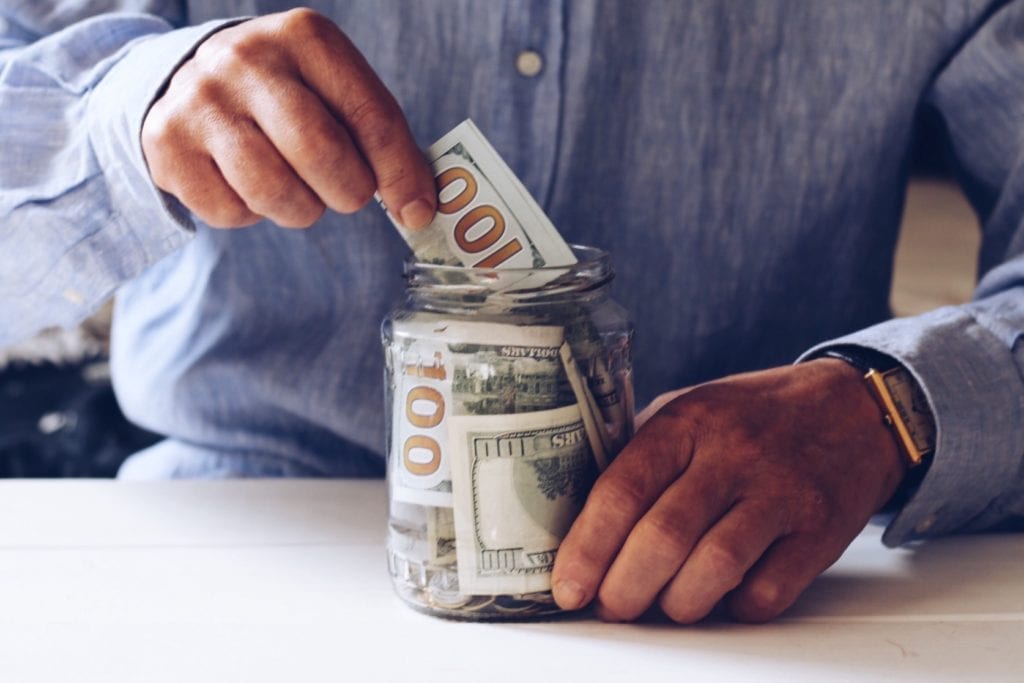 A man puts $100 bills into a jar for savings